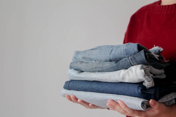 woman holding pile of jeans on white background