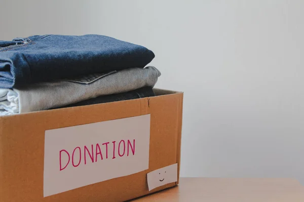 Donation box with clothes on wooden table against white background