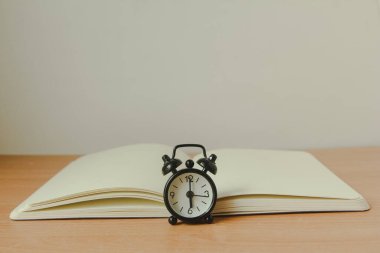 Ahşap zemin üzerinde defter olan siyah çalar saat. Boşluğu kopyala.