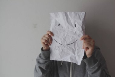 Yüzünde gülen yüz ifadesi olan bir kadın gri bir arka plan, depresyon, akıl sağlığı, maskeleme duyguları....