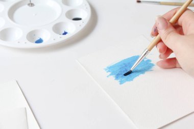 Closeup of women's hand with brush drawing on notepad. creation process of watercolor painting, hobby, selflove.