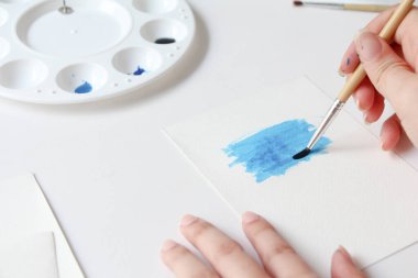 Closeup of women's hand with brush drawing on notepad. creation process of watercolor painting, hobby, selflove.
