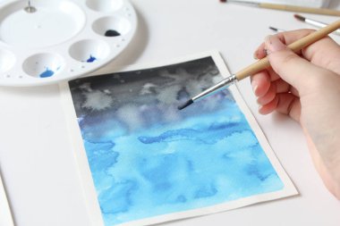 Not defterine fırça darbeleriyle kadın elinin yakın çekimi. suluboya resim yapma, hobi, kendini sevme süreci.