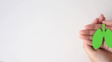 Ahşap masa arkasında kağıt yeşil ciğer tutan kadın elleri, eko hava kirliliği ve organ bağışı kavramı.