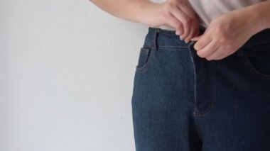 Closeup of female getting dressed wearing jeans standing on gray background.