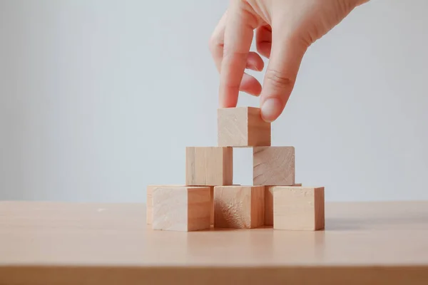 Hand putting wood cube on top of wood block stacking as step stair. business growth to success.