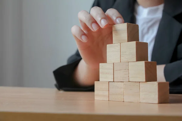 Hand putting wood cube on top of wood block stacking as step stair. business growth to success.