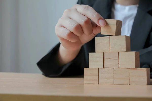 Hand putting wood cube on top of wood block stacking as step stair. business growth to success.