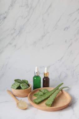Fresh Aloe vera leaves in wooden bowl with slices and gel in wooden spoon. on white marble background. hair care and skin care concept.