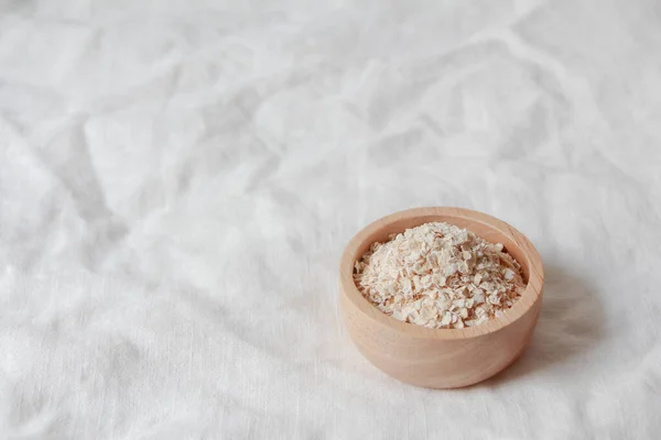 Rolled oats or oat flakes in wooden bowl on fabric  background. Healthy lifestyle, healthy eating, vegan food concept