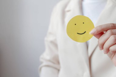 Woman hands holding yellow smile face paper, good feedback rating,think positive, customer review, assessment, world mental health day, Compliment Day.
