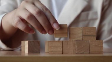 Hand putting wood cube on top of wood block stacking as step stair. business growth to success.