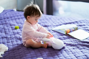 Pembe elbiseli bir bebek, eğitici bir oyuncakla yatak örtüsünde oturuyor.