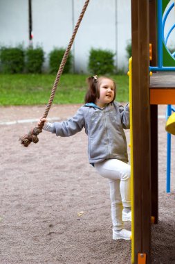 Oyun parkında at kuyruklu şirin bir kız çocuğu koşuyor, tırmanıyor, salıncakta sallanıyor ve kayıyor. Açık havada aktif boş zaman