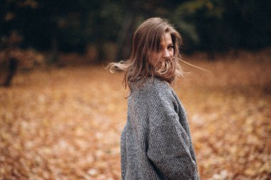 Parkta sonbaharda uzun saçlı güzel bir sarışın kız yürüyor. Sonbahar portresi