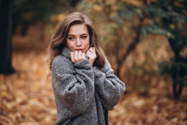 Parkta sonbaharda uzun saçlı güzel bir sarışın kız yürüyor. Sonbahar portresi