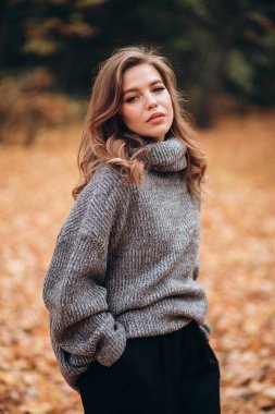 Parkta sonbaharda uzun saçlı güzel bir sarışın kız yürüyor. Sonbahar portresi