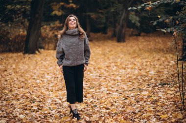 Parkta sonbaharda uzun saçlı güzel bir sarışın kız yürüyor. Sonbahar portresi