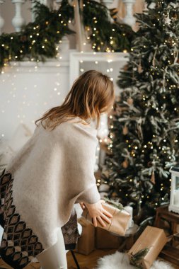 Kış tatili ile kutlanan paketlenmiş Noel hediyelerine odaklan, hazırlık hediyelerini hatırlat, dekore edilmiş ağacın yanında poz ver.