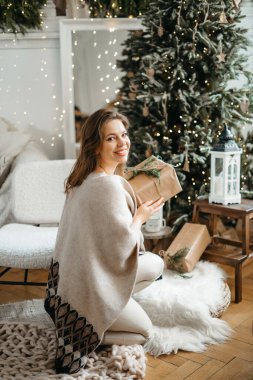 Kış tatili ile kutlanan paketlenmiş Noel hediyelerine odaklan, hazırlık hediyelerini hatırlat, dekore edilmiş ağacın yanında poz ver.