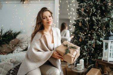Rahat kış kıyafetleri içinde gülümseyen güzel bir kadın kameraya bir hediye kutusu uzatıyor, bir Noel hediyesi hazırlıyor, kış tatilini kutluyor.