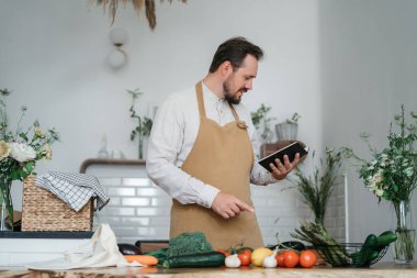 Yeşil malzemeleri ve baharatlı otları olan yakışıklı bir adam mutfakta sağlıklı yemek hazırlıyor.