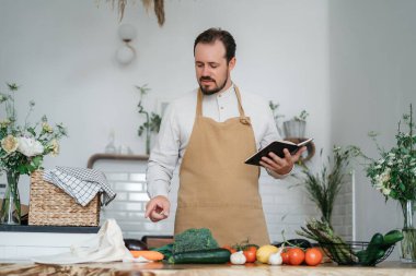 Yeşil malzemeleri ve baharatlı otları olan yakışıklı bir adam mutfakta sağlıklı yemek hazırlıyor.