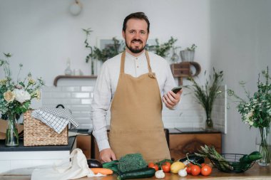 Yeşil malzemeleri ve baharatlı otları olan yakışıklı bir adam mutfakta sağlıklı yemek hazırlıyor.