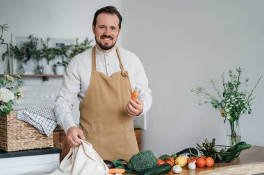 Yeşil malzemeleri ve baharatlı otları olan yakışıklı bir adam mutfakta sağlıklı yemek hazırlıyor.