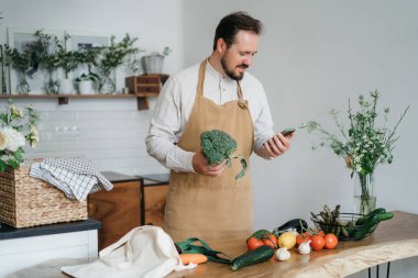Yeşil malzemeleri ve baharatlı otları olan yakışıklı bir adam mutfakta sağlıklı yemek hazırlıyor.