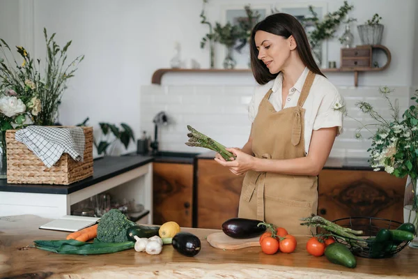 Mulher bonita com ingredientes verdes pensando em cozinhar alimentos saudáveis na cozinha. Conceito de saúde e bem-estar — Fotografia de Stock