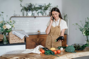 Mutfakta cep telefonu olan genç bir kadın sağlıklı vejetaryen yemekleri pişiriyor.