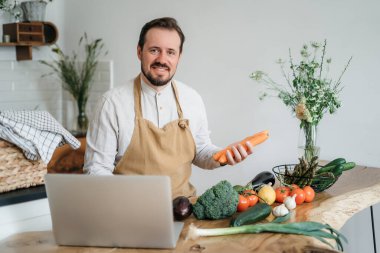 Evdeki mutfakta dizüstü bilgisayarda yemek tarifi arayan bir adam.