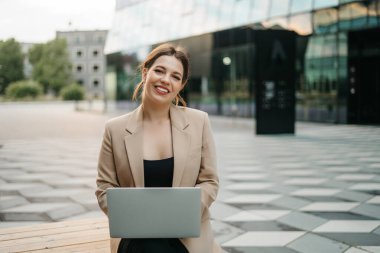 Açık havada dizüstü bilgisayar kullanan mutlu ve çekici bir bayan serbest yazar ya da öğrenci. Bilgisayarlı neşeli kadın kameraya bakıyor ve gülümsüyor.