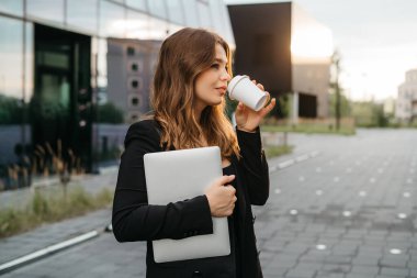 Dışarıda telefon ve kahve fincanıyla duran genç ve neşeli bir kadının hayat tarzı portresi. Kentsel iş seyahati ve ulaşım kavramı