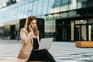 Dışarıda dizüstü bilgisayar kullanarak oturan çekici iş kadınının portresi.