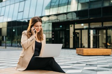 Dışarıda dizüstü bilgisayar kullanarak oturan çekici iş kadınının portresi.