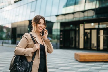 Dışarıda telefon ve sırt çantasıyla duran genç ve neşeli bir kadının hayat tarzı portresi. Şehir iş seyahati ve ulaşım kavramı