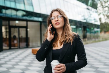 Gülümseyen mutlu bayan girişimci küçük işletme sahibi şehir merkezindeki akıllı telefondan konuşuyor, akıllı günlük kıyafet giymiş pozitif kadın ofis çalışanı şehir caddesinde telefonda sohbet ediyor.. 
