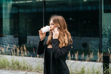 Telefonda konuşan, şehrin arka planında gülümseyen, kahve içen, seyahat konsepti olan çekici, pozitif sarışın bir kadının portresi. Yüksek kalite fotoğraf