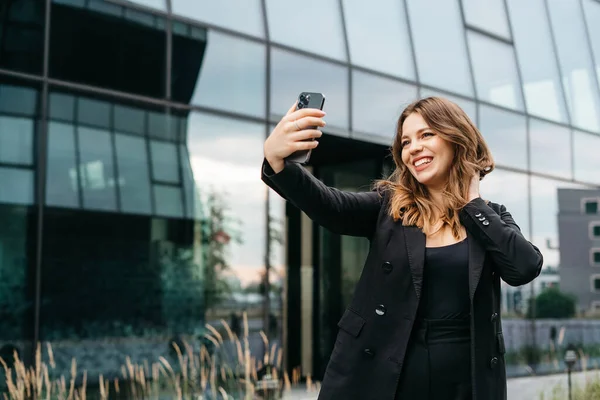 Happy female using mobile app on smartphone for making video call, waving hand and greeting friends or family, talking via video connection, stay in touch on the distance.