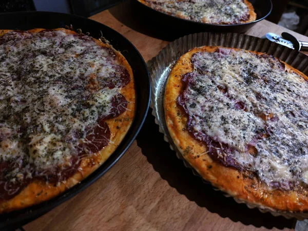 Ahşap bir paspasın üzerinde üç büyük pizza, fotoğraf.