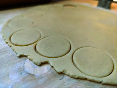 Kurabiyeler için yuvarlanmış hamurlar ahşap bir oklava, bir tabak kurabiye, kesilmiş hamur parçaları, fotoğraf.