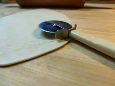 Close-up view of a cutting wheel for dough on a wooden background with flour. Dough roll in the background. side view, photo