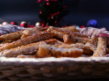View of puff pastry salty sticks sprinkled with cumin and sesame seeds in a wicker basket, with Christmas decorations in the background, photo