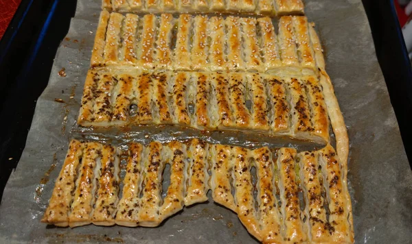 Puff pastry salty sprinkles with cumin and sesame seeds on a baking sheet, photo