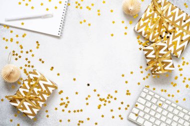 Beyaz klavye, hediyeler, not defteri, kalem, altın konfeti ve gri desenli arka planda kağıt süslemeler. Noel işi konsepti. Hediyelerle dolu bir tatil yeri. Düz konum, üst görünüm, kopyalama alanı
