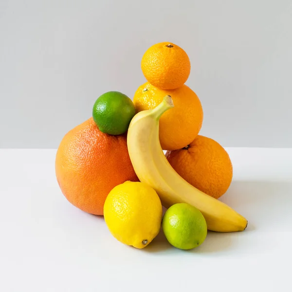 Jeruk, jeruk, pisang, kapur, jeruk keprok dan lemon seimbang pada latar belakang abu-abu. Kuning, oranye dan hijau buah-buahan dengan vitamin C dan antioksidan. Diet vegetarian sehat Stok Gambar