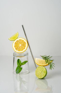 Taze limonata konsepti. Limon ve limon dilimleri, nane yaprağı, biberiye, cam ve yeniden kullanılabilir çelik kamış. Ev yapımı yaz içeceği. Boşluğu kopyala