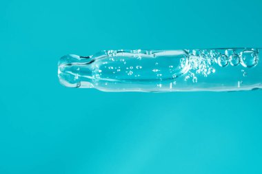 Şeffaf yüz serumlu cam pipet ve hafif turkuaz arka planda kabarcıklar. Sağlıklı cilt bakımı. Yenilik kozmetik ürün makrosu. Hyaluronik asit içeren sıvı jel. Güzellik konsepti
